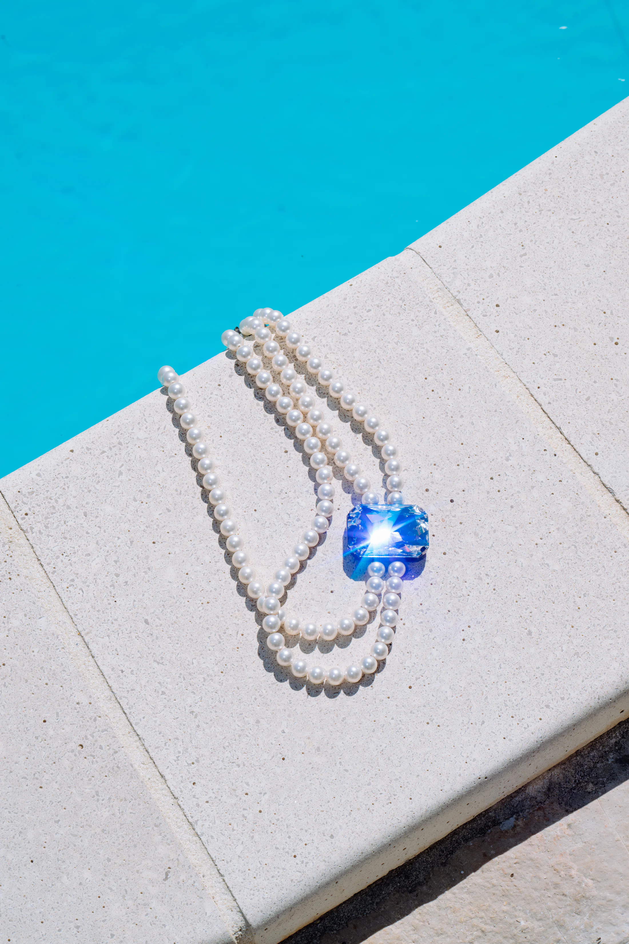 Pearl necklace and blue gemstone beside a pool