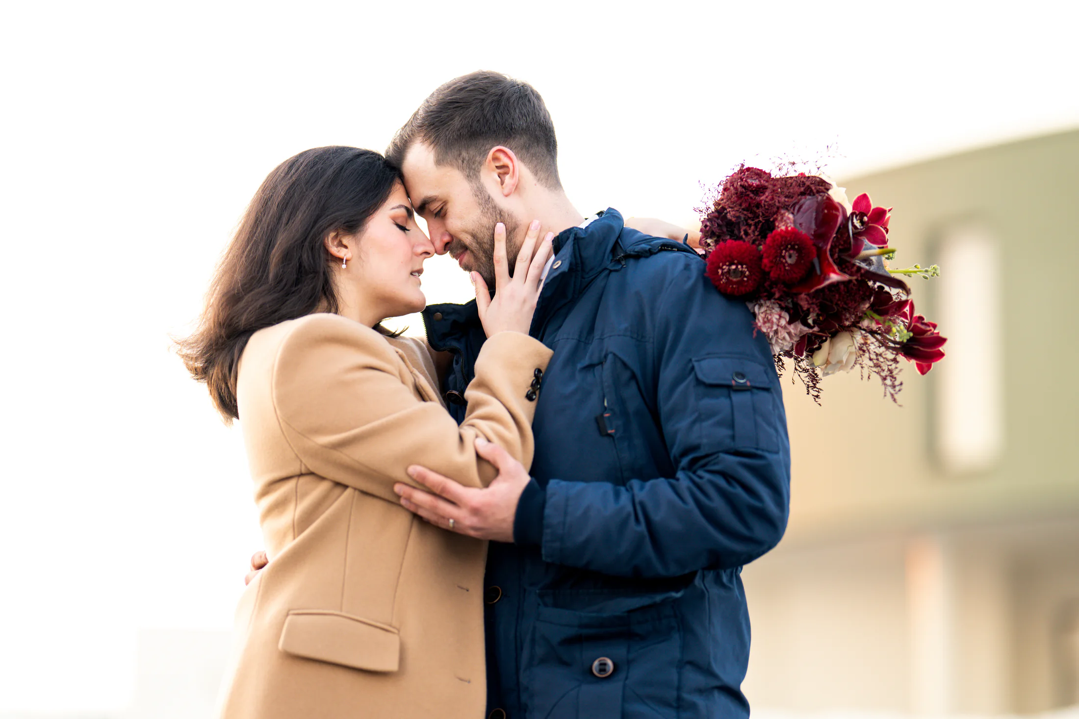 Winter bride and groom embracing with a burgundy bouquet