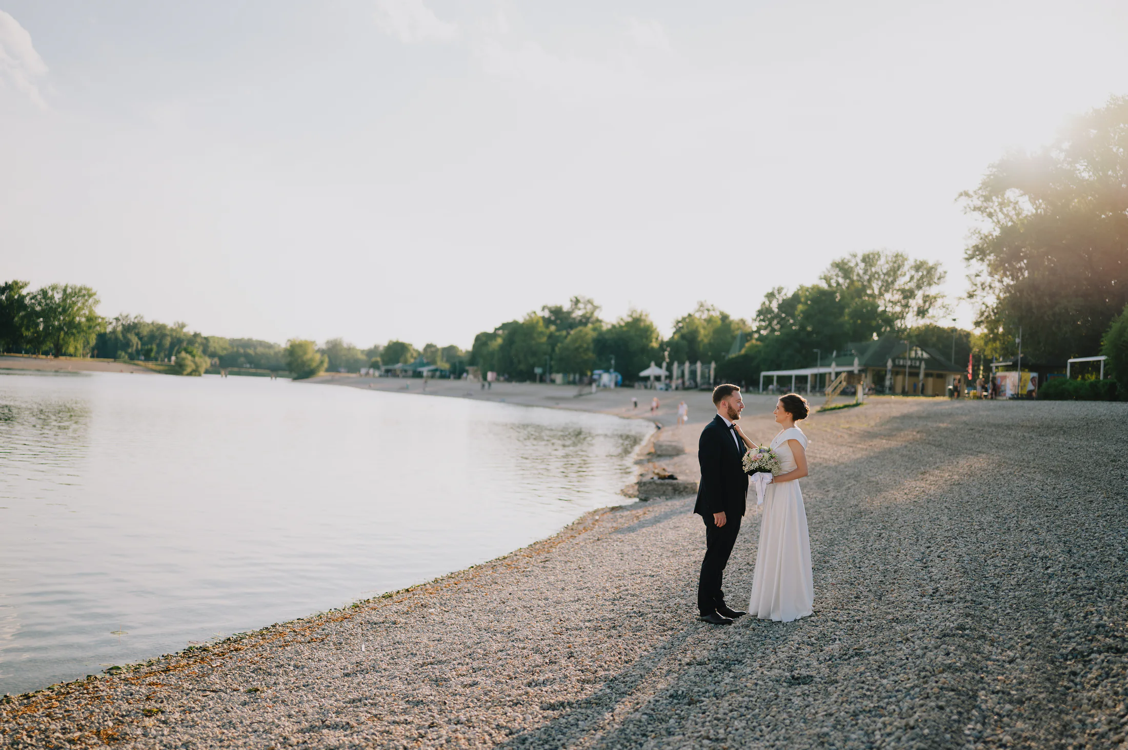 Bride and groom standing on a lakeside shore at golden hour