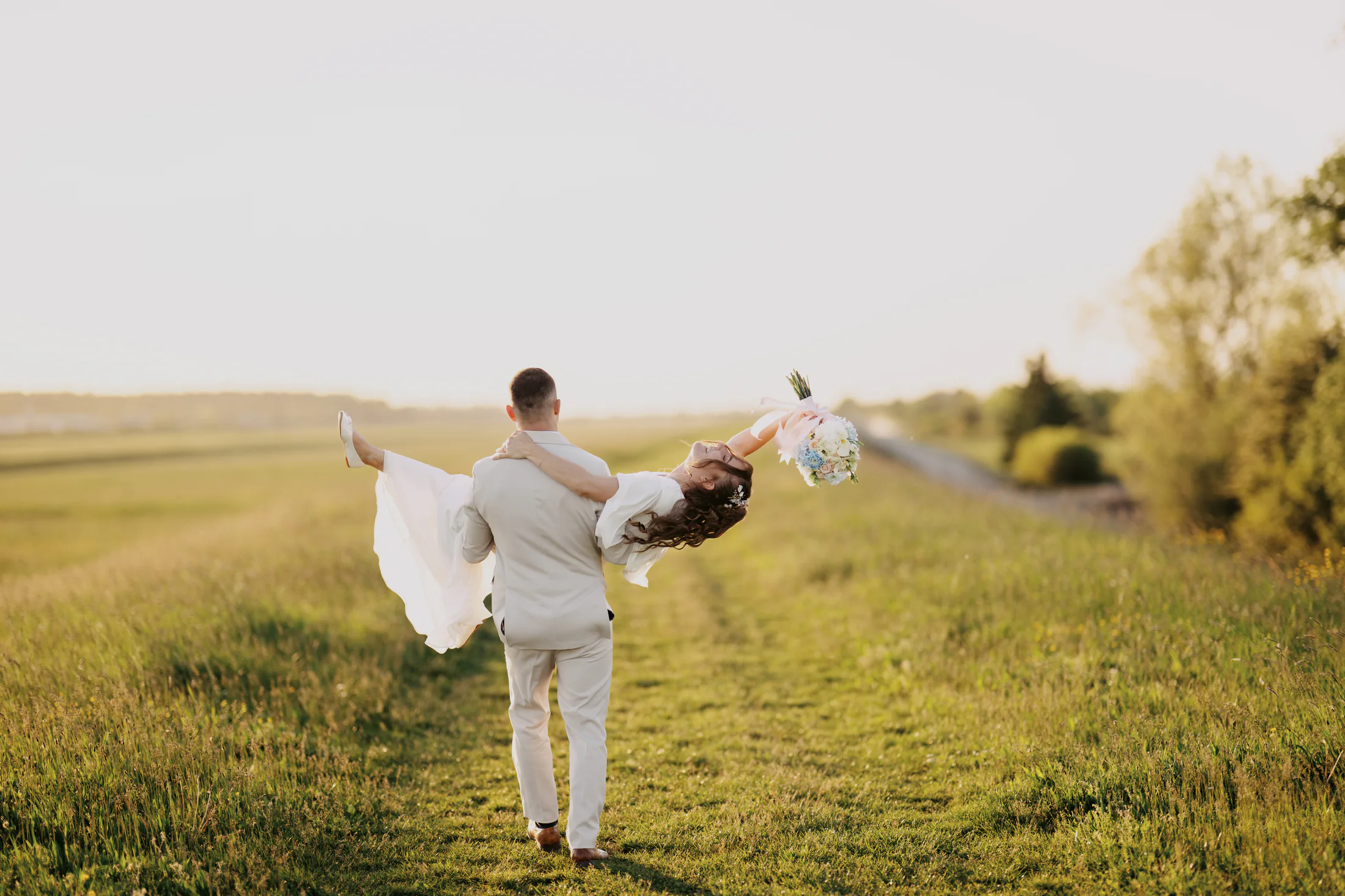Groom carrying the bride through a sunlit field