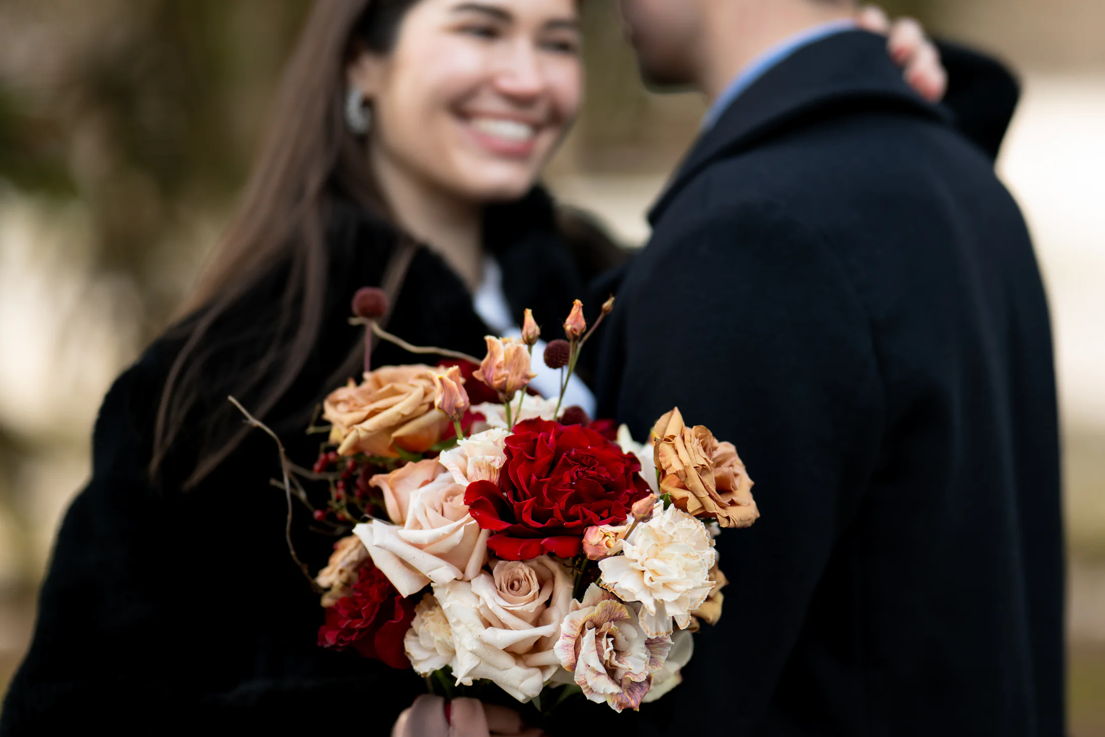 Deep red bridal bouquet with a couple softly blurred behind